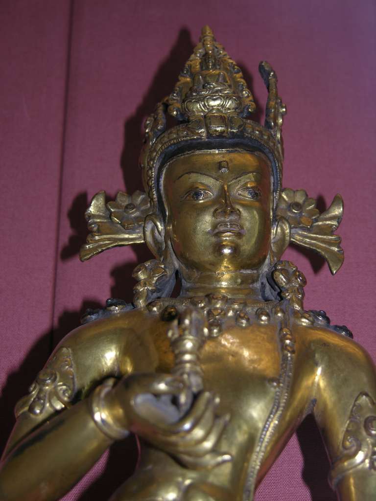 British Museum Top 20 Buddhism 16-2 Vajrasattva Close Up 16. Vajrasattva � Nepal, 15C AD, 52cm high. Here is a close up of Vajrasattva holding the vajra and bell in his hands, has elaborate jewelry, and is inset with semi-precious stones. In Vajrasattva's crown is the seated figure of the Akshobhya, the Tathagata Meditation Buddha of the East.